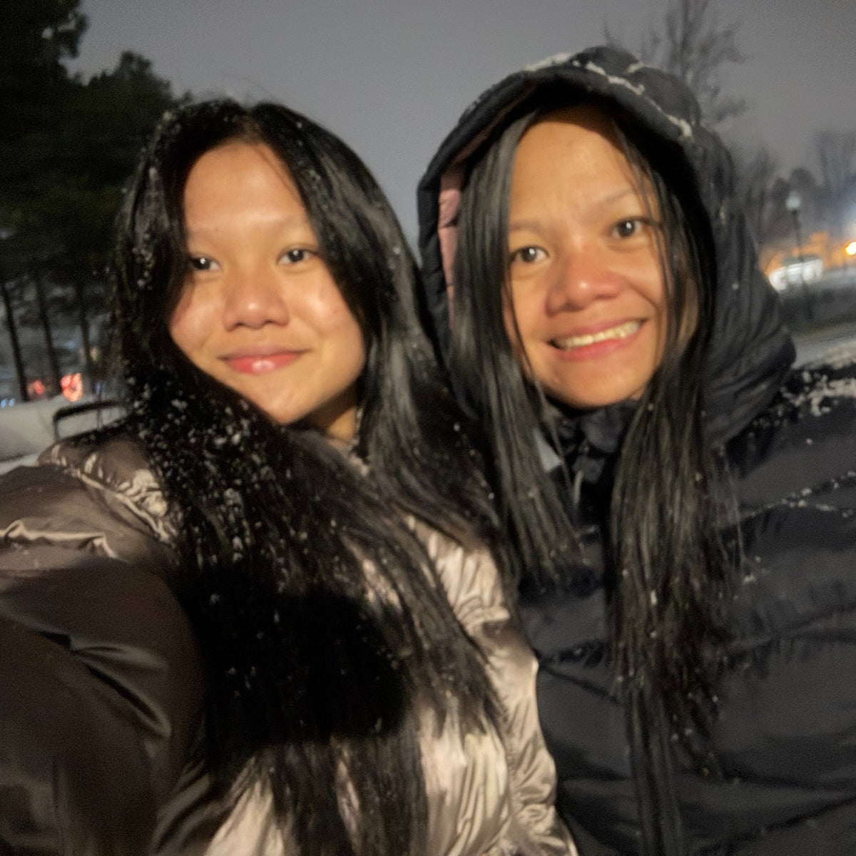 Two women in winter coats standing outdoors at night.