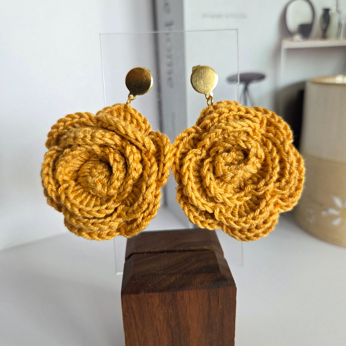 Yellow crochet earrings on a wooden block with a blurred background