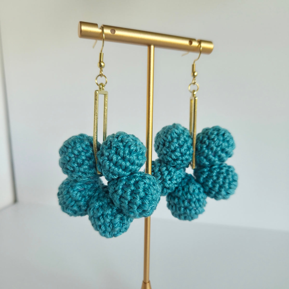 Teal crocheted earrings on a gold earring stand against a white background