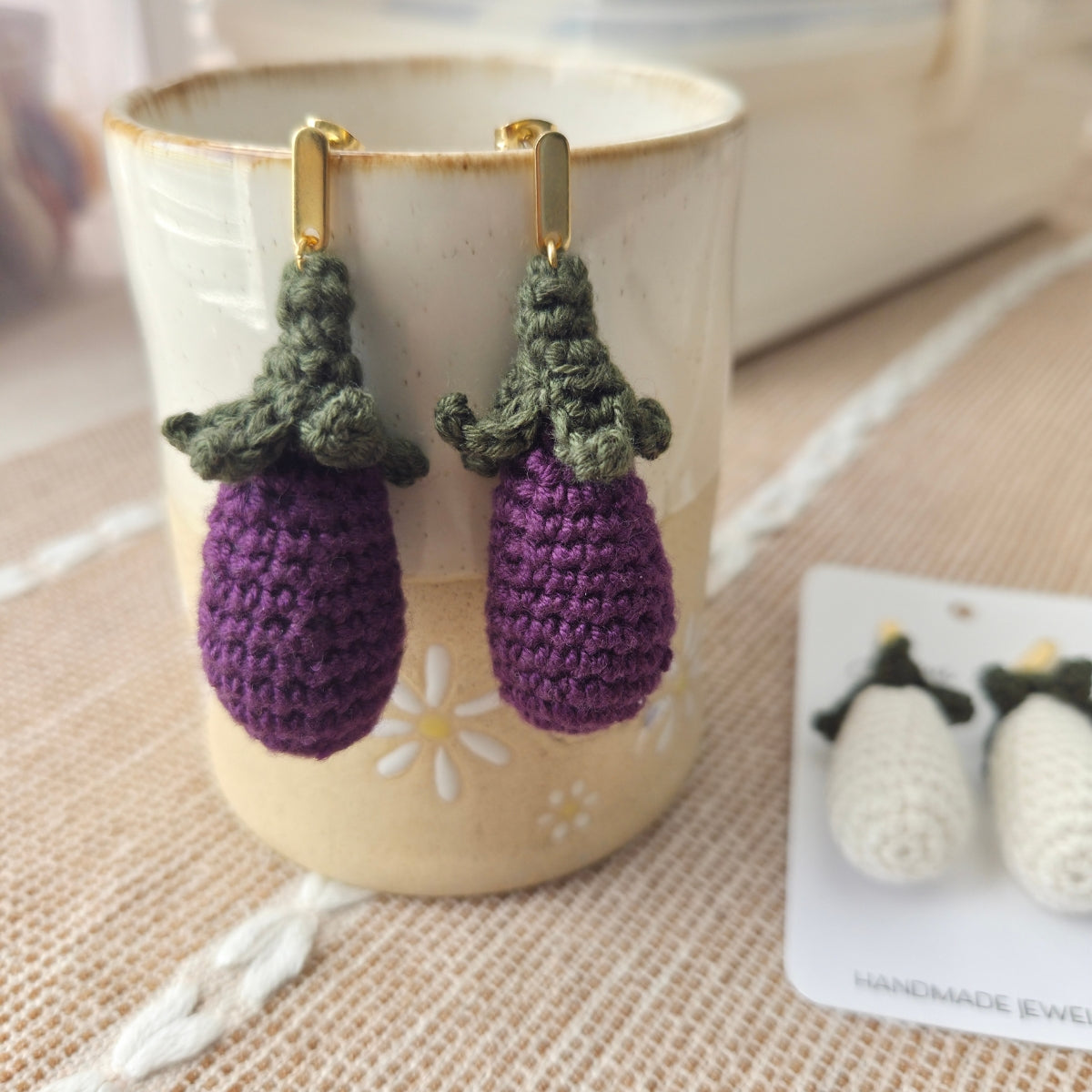 Crocheted eggplant earrings on a cup with a blurred background