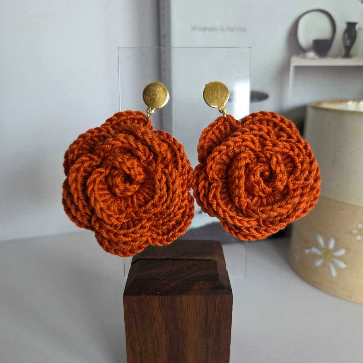 Orange crochet earrings in golden studs on a wooden block with a blurred background
