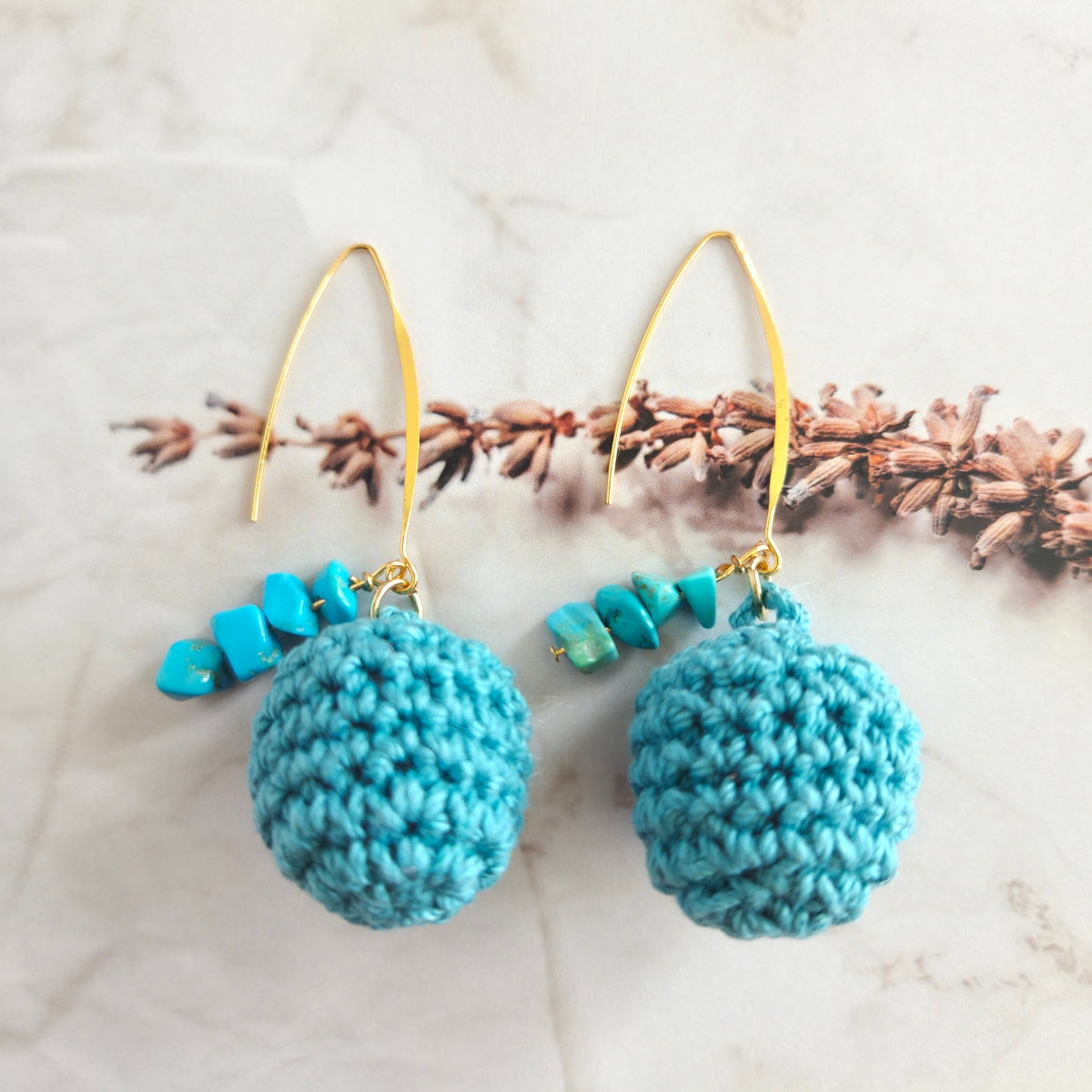 Warm teal crocheted ball drop earrings with gold hooks on a light background