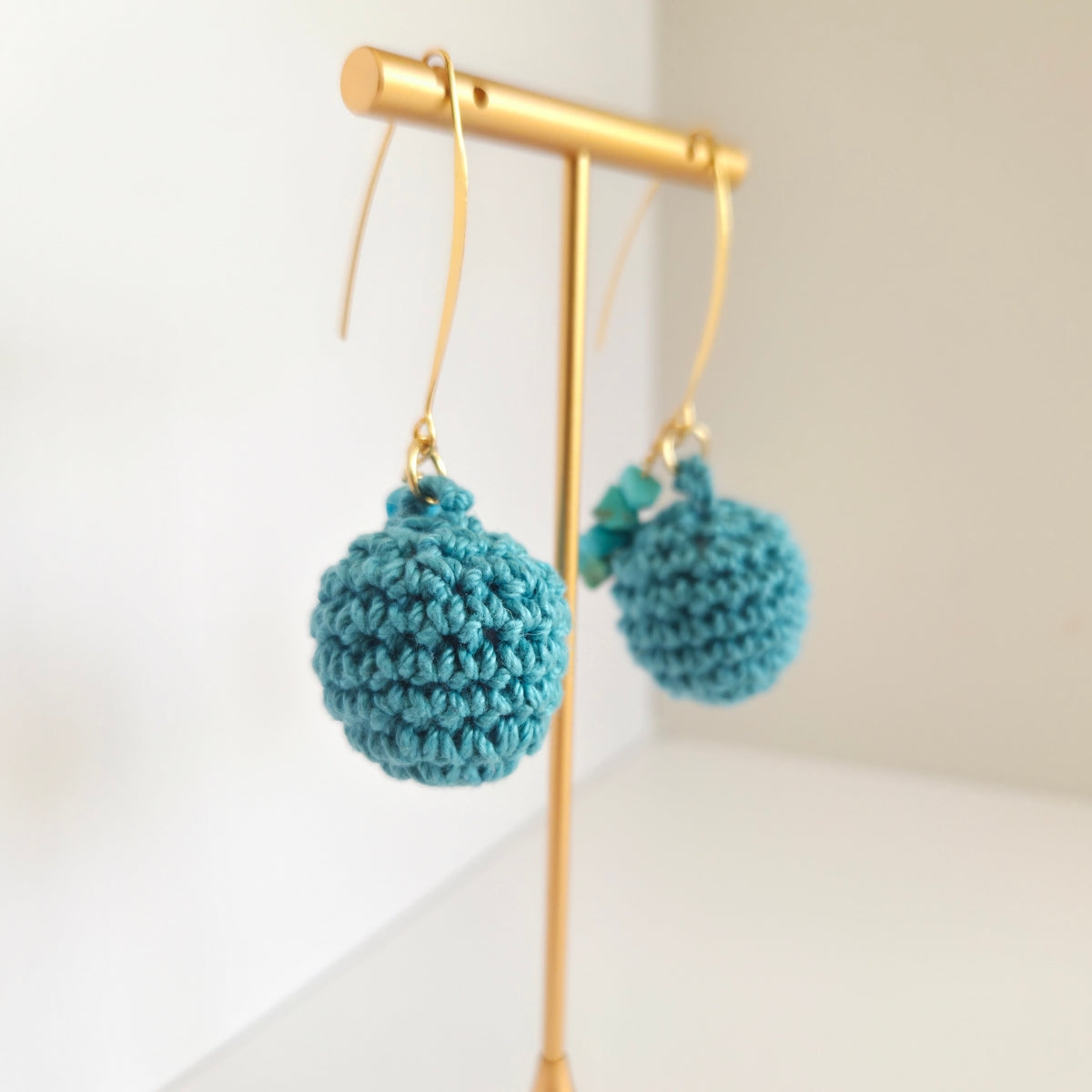 Teal crochet earrings on a gold earring stand on a white background
