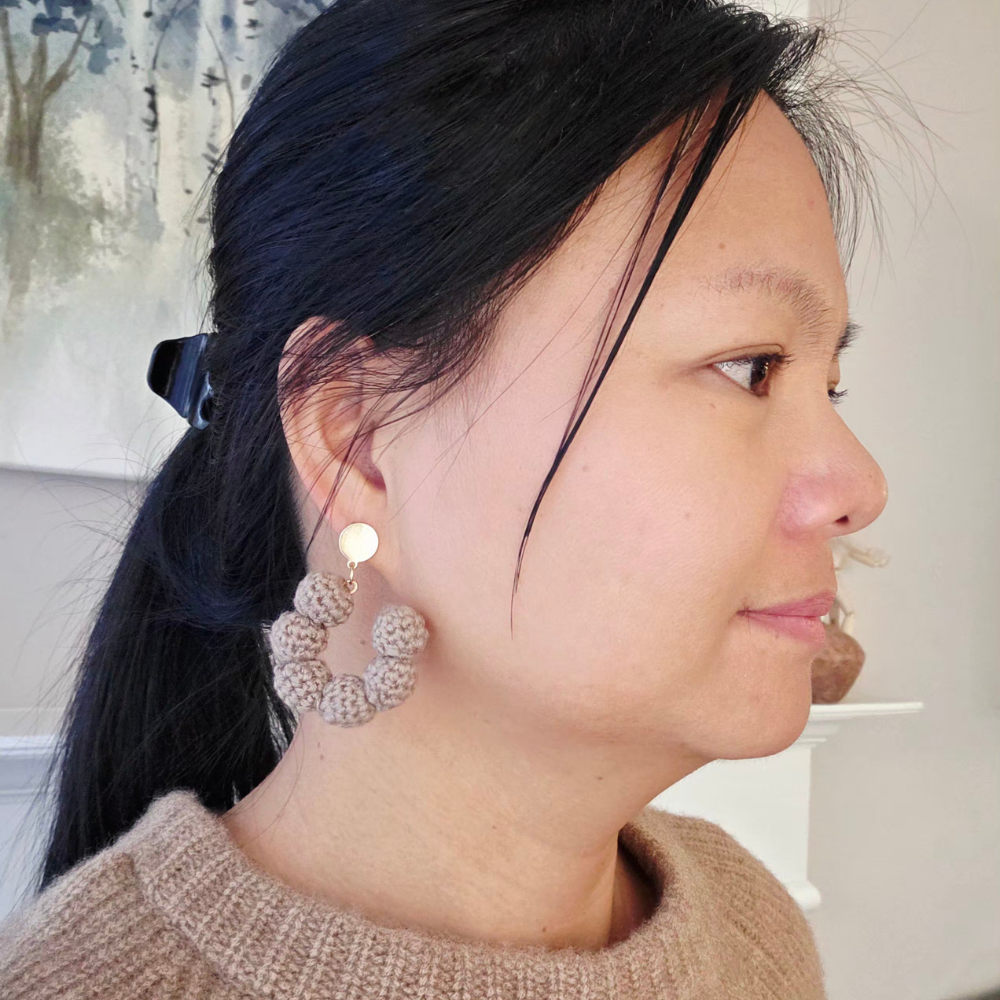a woman wearing a crochet neutral hoop earrings on a beige background