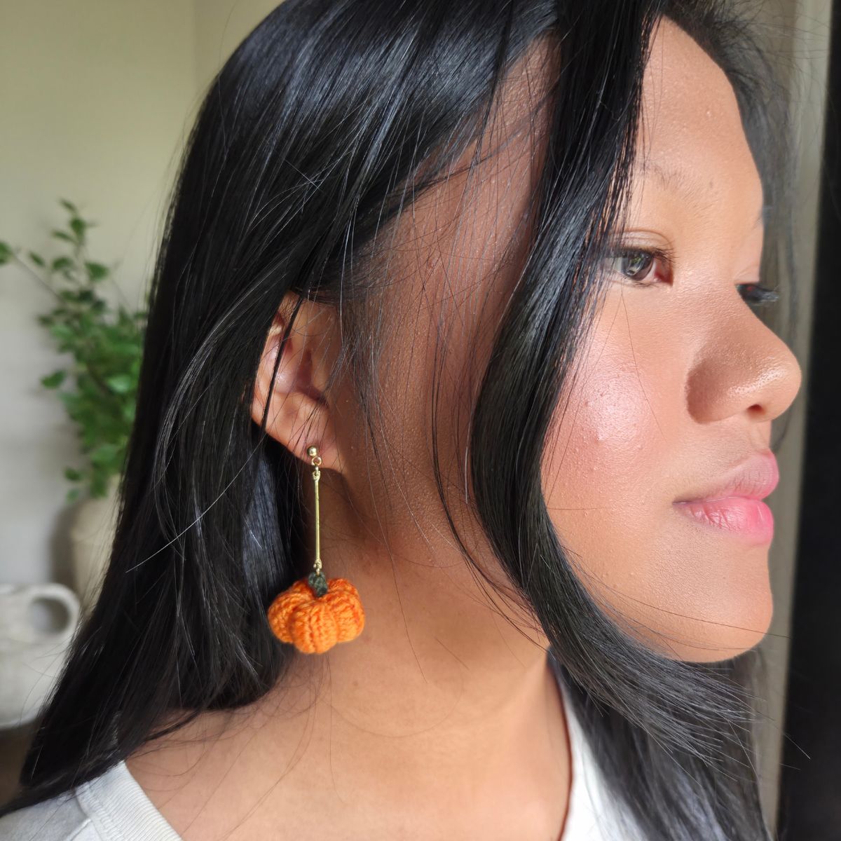 Woman wearing orange crochet pumpkin earrings with a neutral background