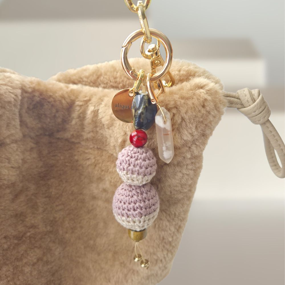 Crocheted keychain with beads hanging from a beige bag.