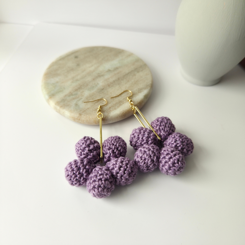 Purple crocheted earrings on a marble coaster with a white background