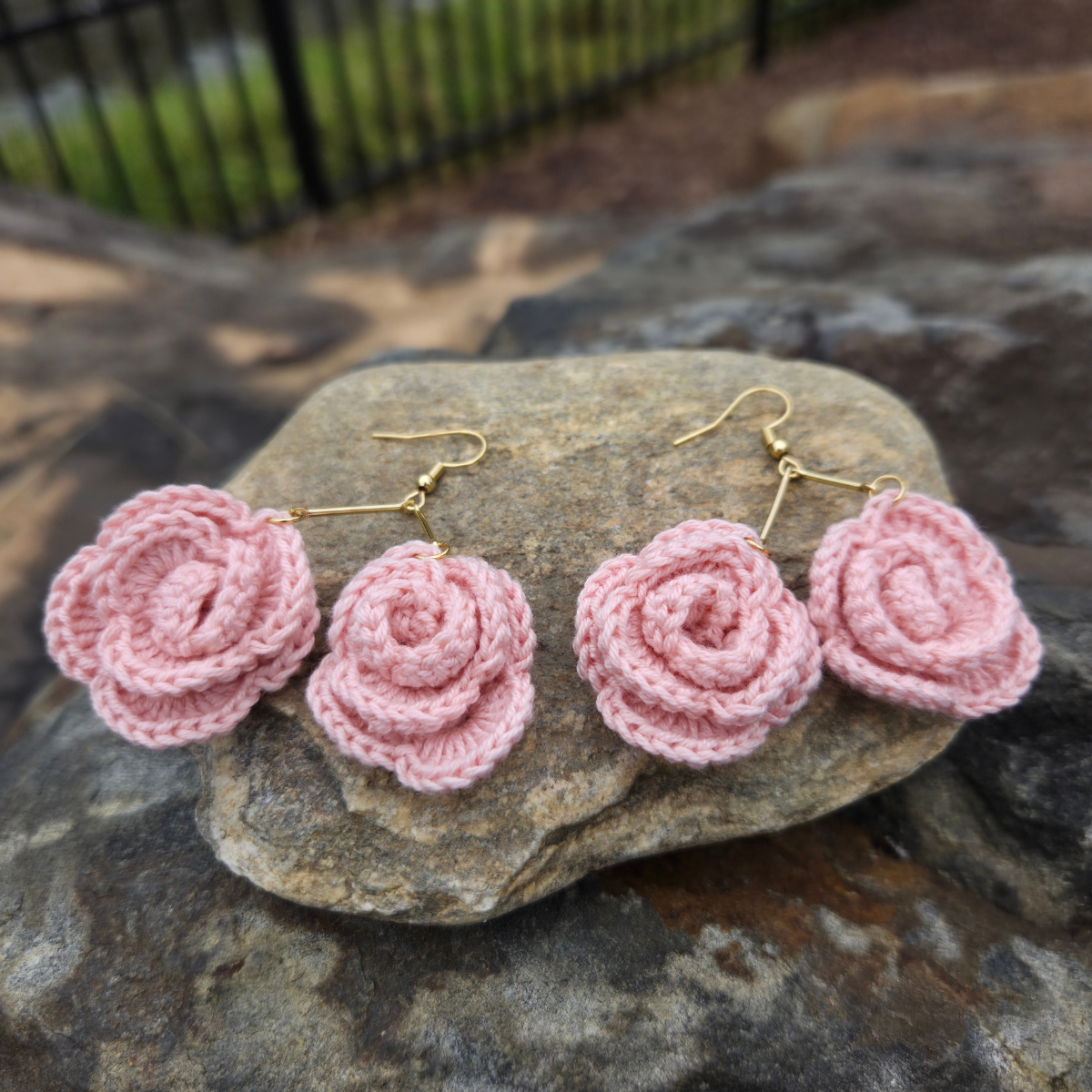 Peach crocheted rose earrings on a stone surface with a blurred natural background