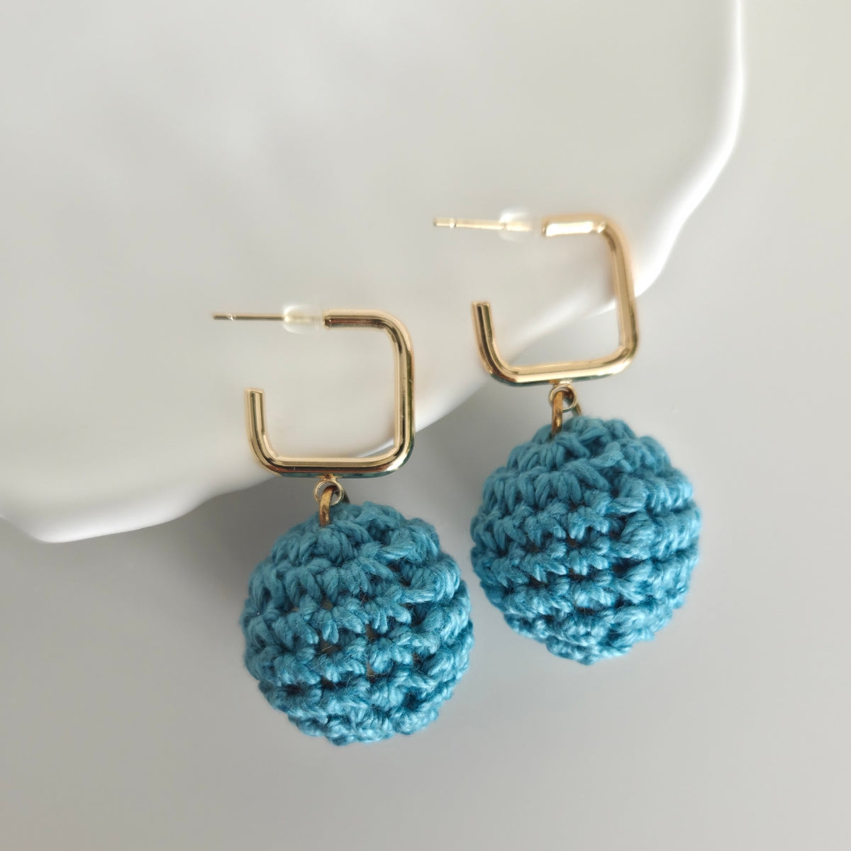 Warm teal crocheted earrings with gold hooks on a white background