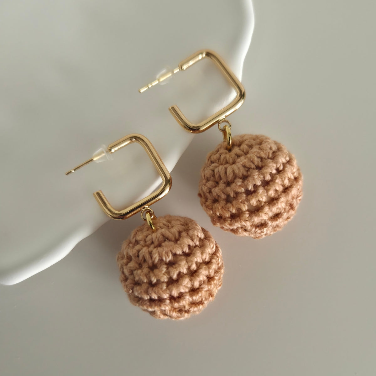 Pair of gold hoop earrings with brown spherical charms on a white surface.