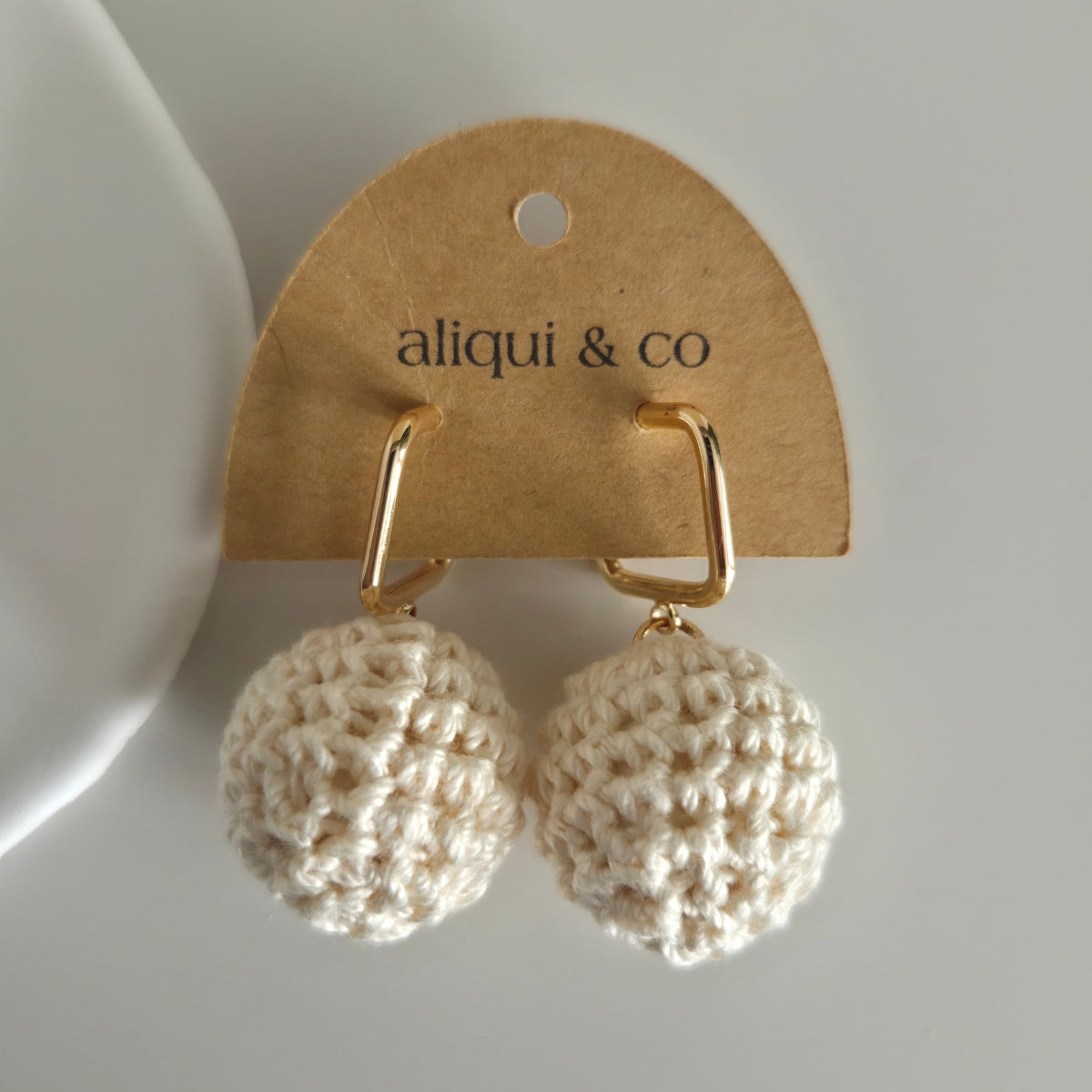 Beige crochet earrings on a 'aliqui & co' branded card against a white background