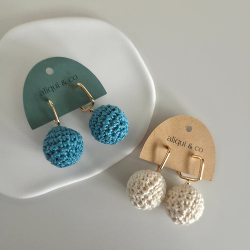 Pair of blue and beige textured ball earrings on aliqui & co branded cards.