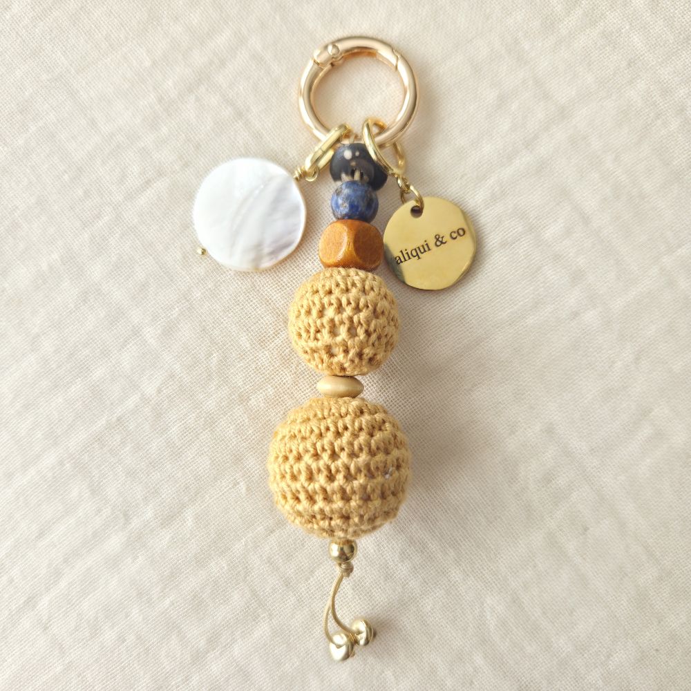 Beaded crochet keychain with gold clasp on a textured beige background