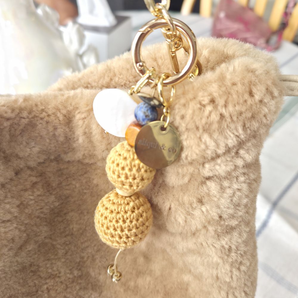 Yellow crochet keychain with beads and charms attached to a beige textured surface