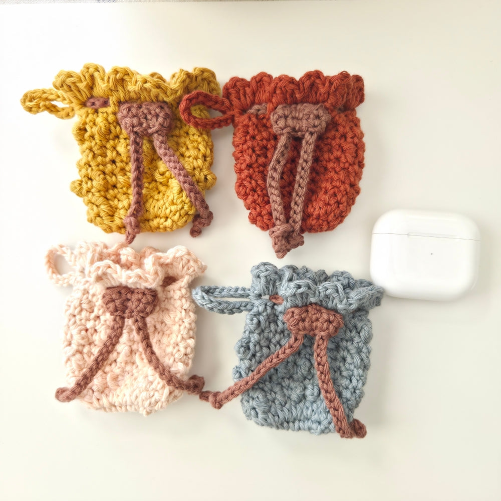 Four crocheted earbud pouches in yellow, orange, pink, and blue on a white background.