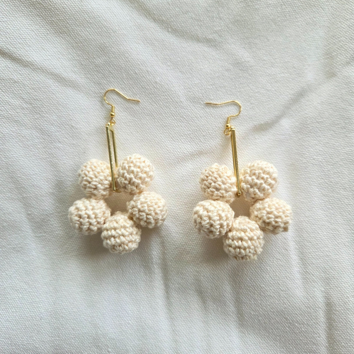 Pair of cream crochet ball earrings on a light fabric background