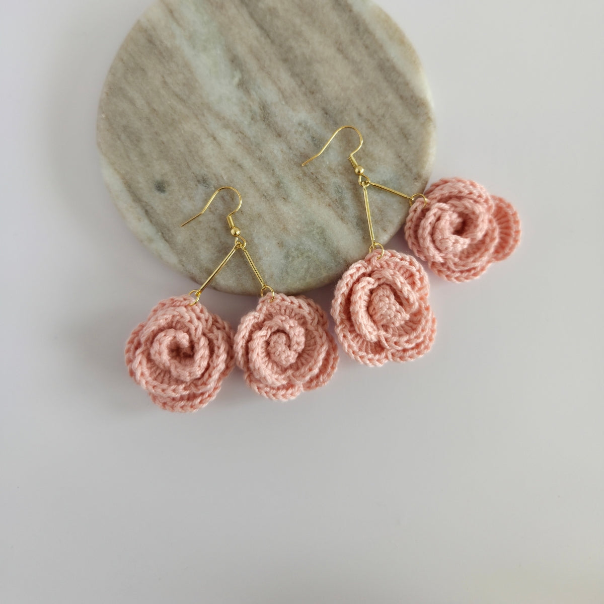 Light peach  mini-rose-shaped earrings on a stone surface