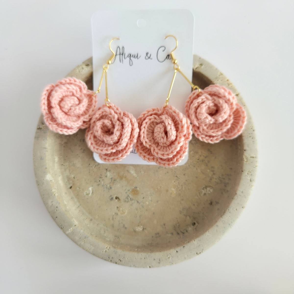 Pink mini rose dangle earrings on a white card with 'Alqui & Co' branding, displayed on a textured beige plate.