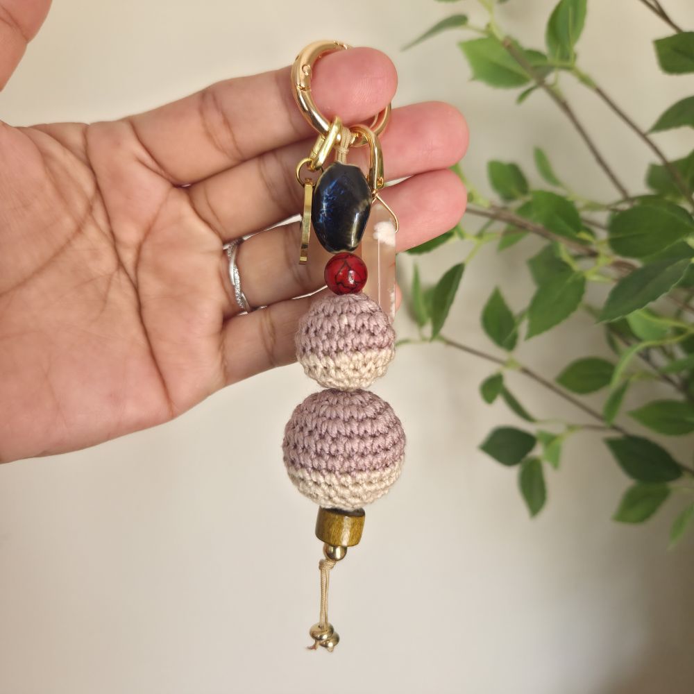 Hand holding a decorative keychain with beads against a blurred natural background