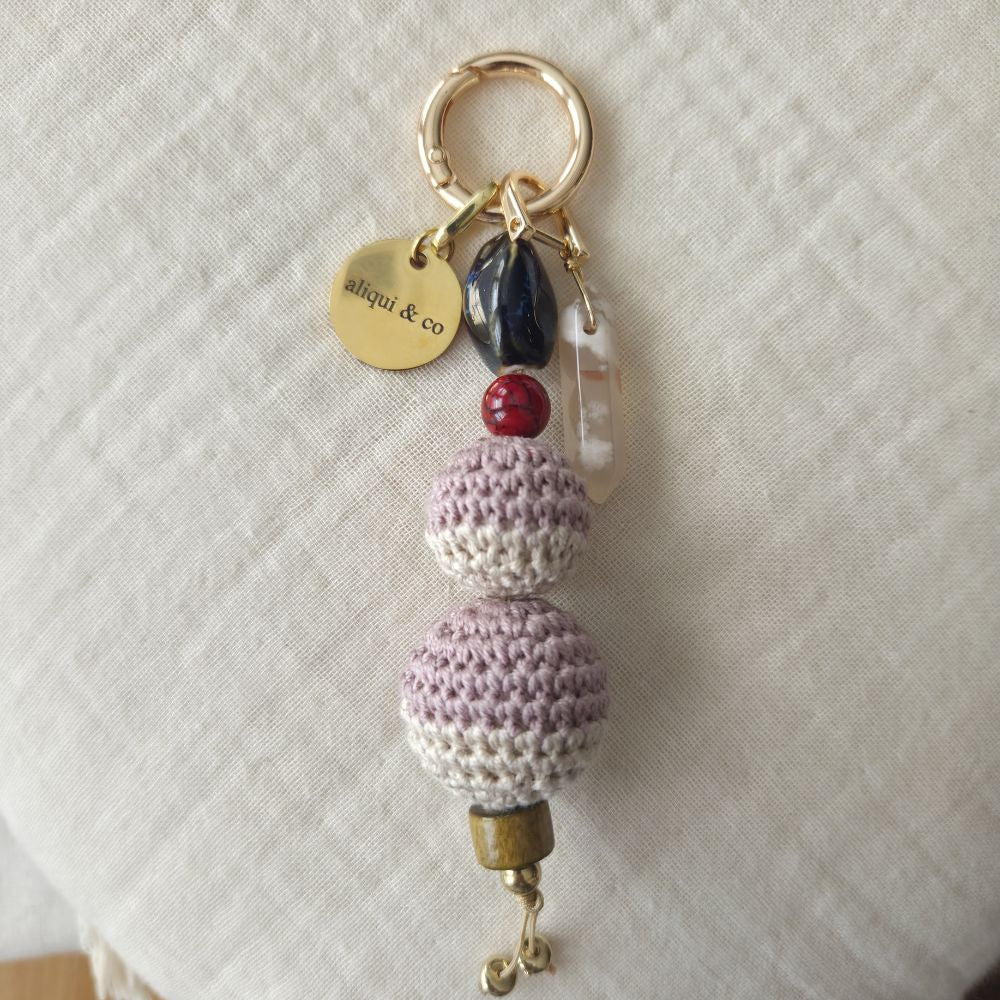 Crocheted keychain with beads and a gold tag on a light fabric background