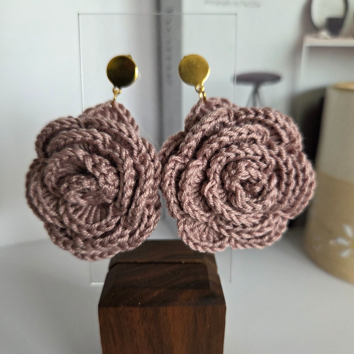 Pair of dusty mauve pink handmade crochet flower earrings on a wooden block with a blurred background