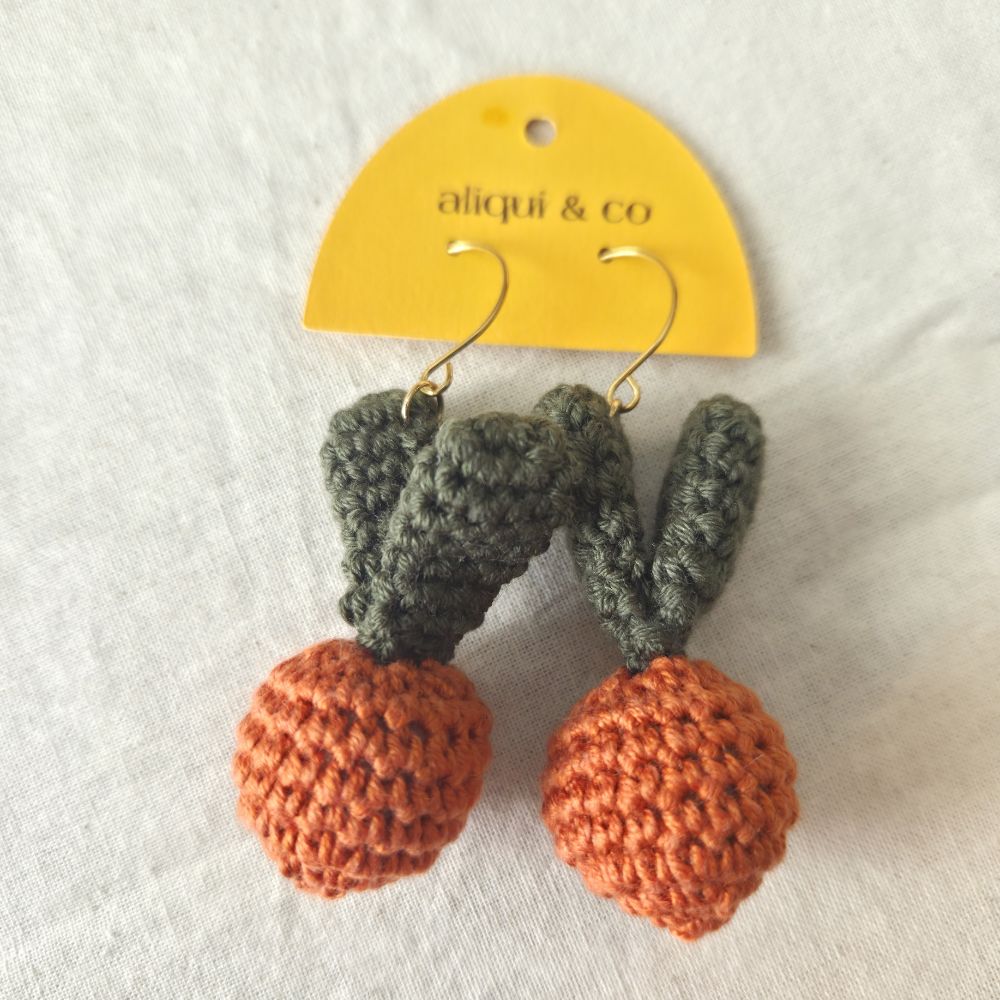 Crocheted carrot earrings with green leaves  on a 'aliqui & co' card.