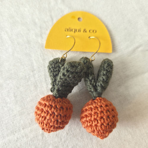 Crocheted carrot earrings with green leaves  on a 'aliqui & co' card.