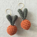 Pair of crocheted carrot earrings on a light gray background