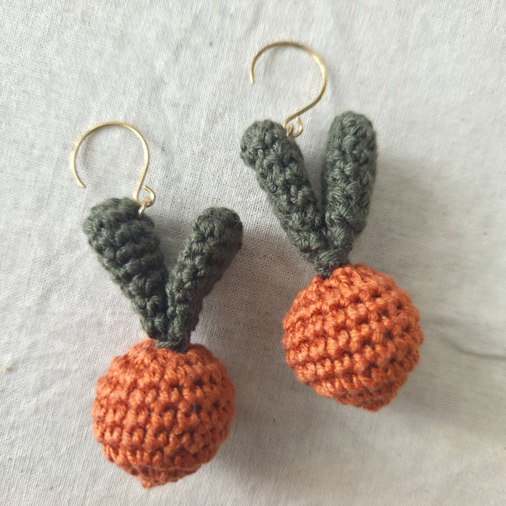 Pair of crocheted carrot earrings on a light gray background