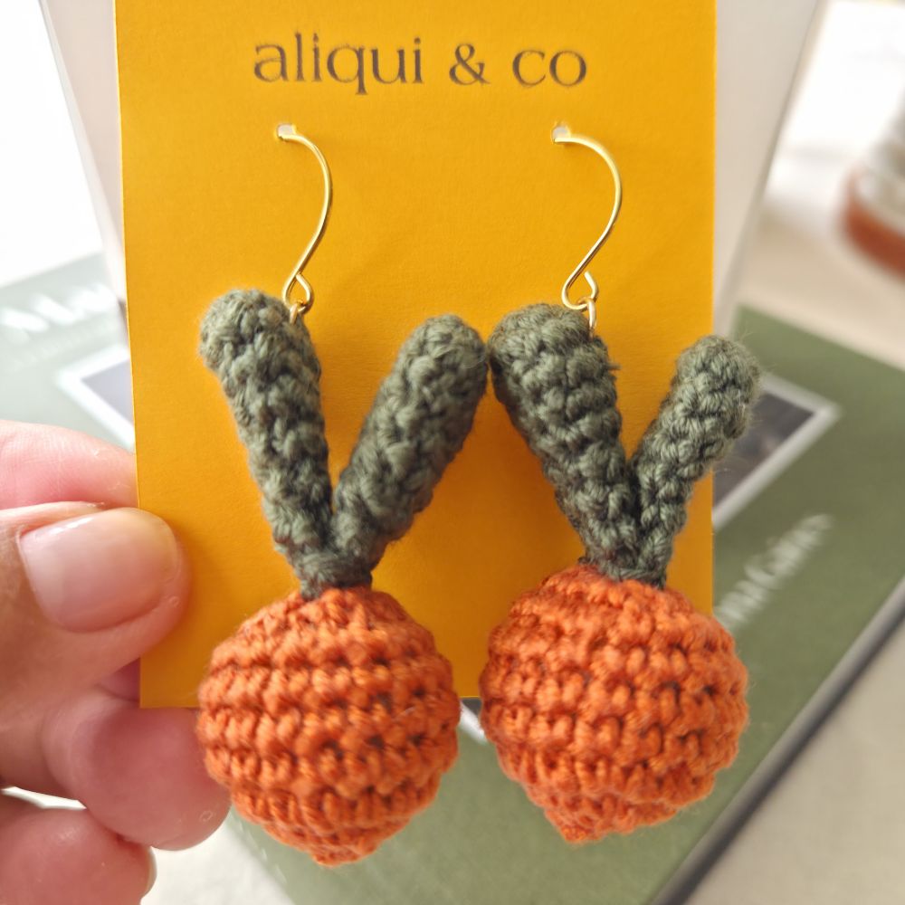 Crocheted carrot-shaped earrings on a card with 'aliqui & co' branding.
