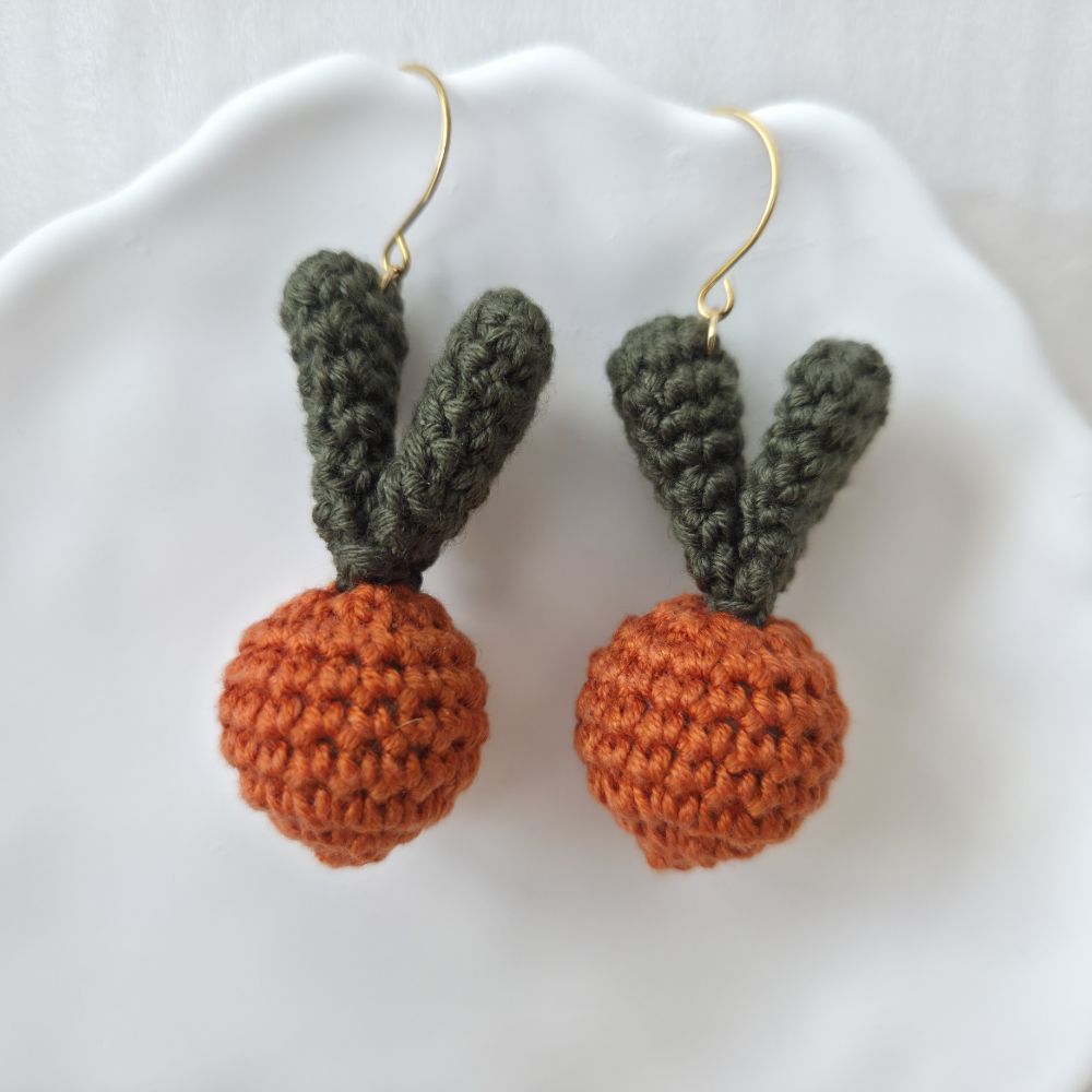 Crocheted carrot earrings on a white surface