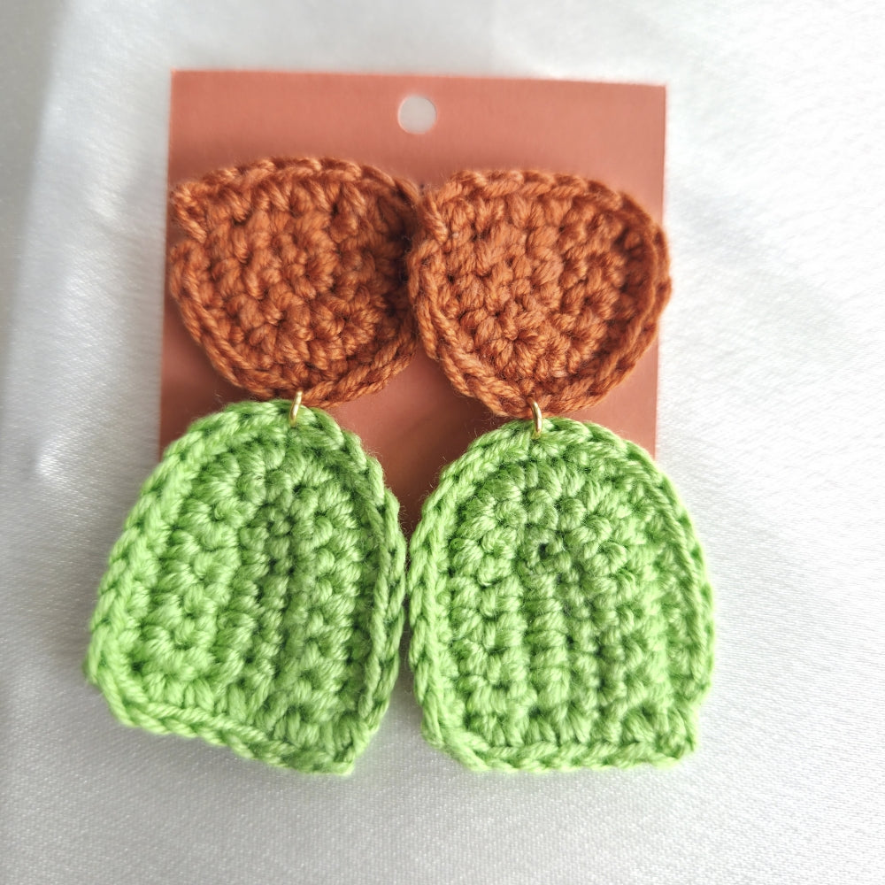 Crocheted earrings with orange and green colors on a pink card.