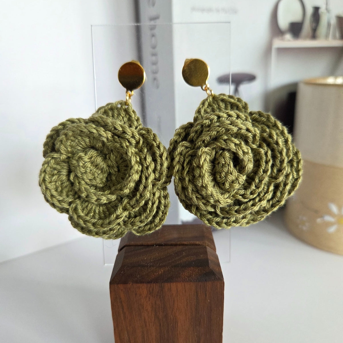 Green crochet earrings on a wooden block with a blurred background
