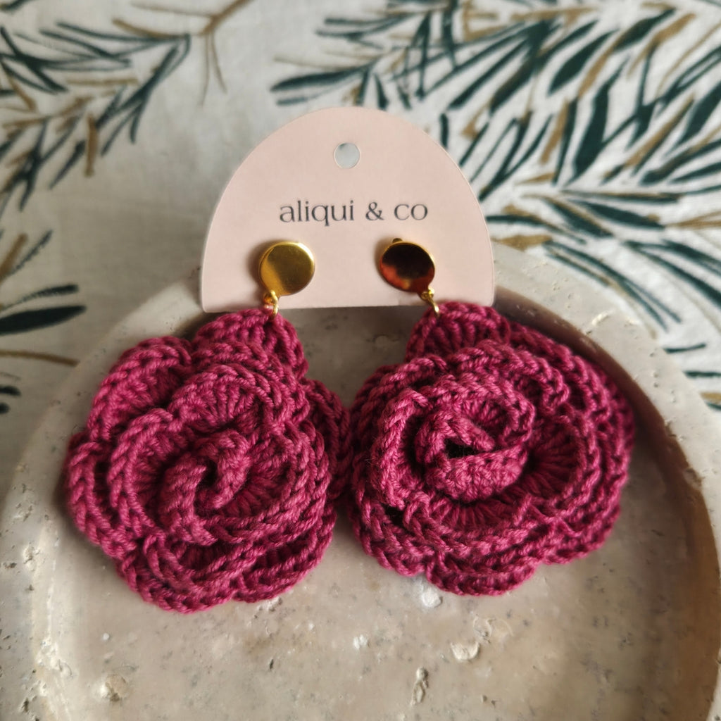 Pink crochet earrings on a pink 'aliqui & co' card with a leafy background.