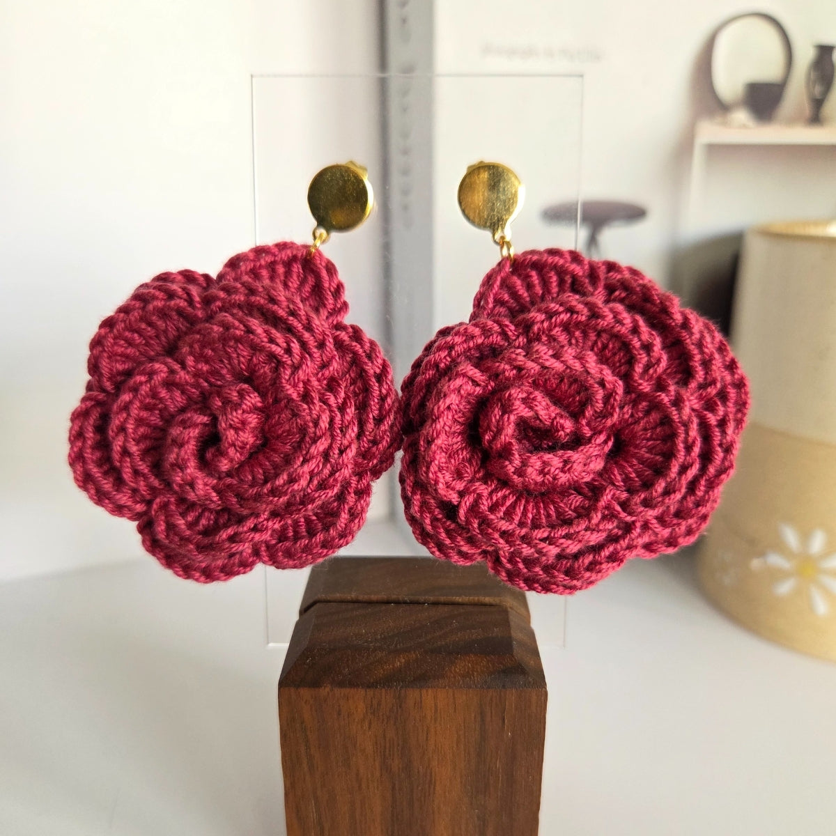 Marsala pink flower-shaped earrings on a wooden block with a blurred background