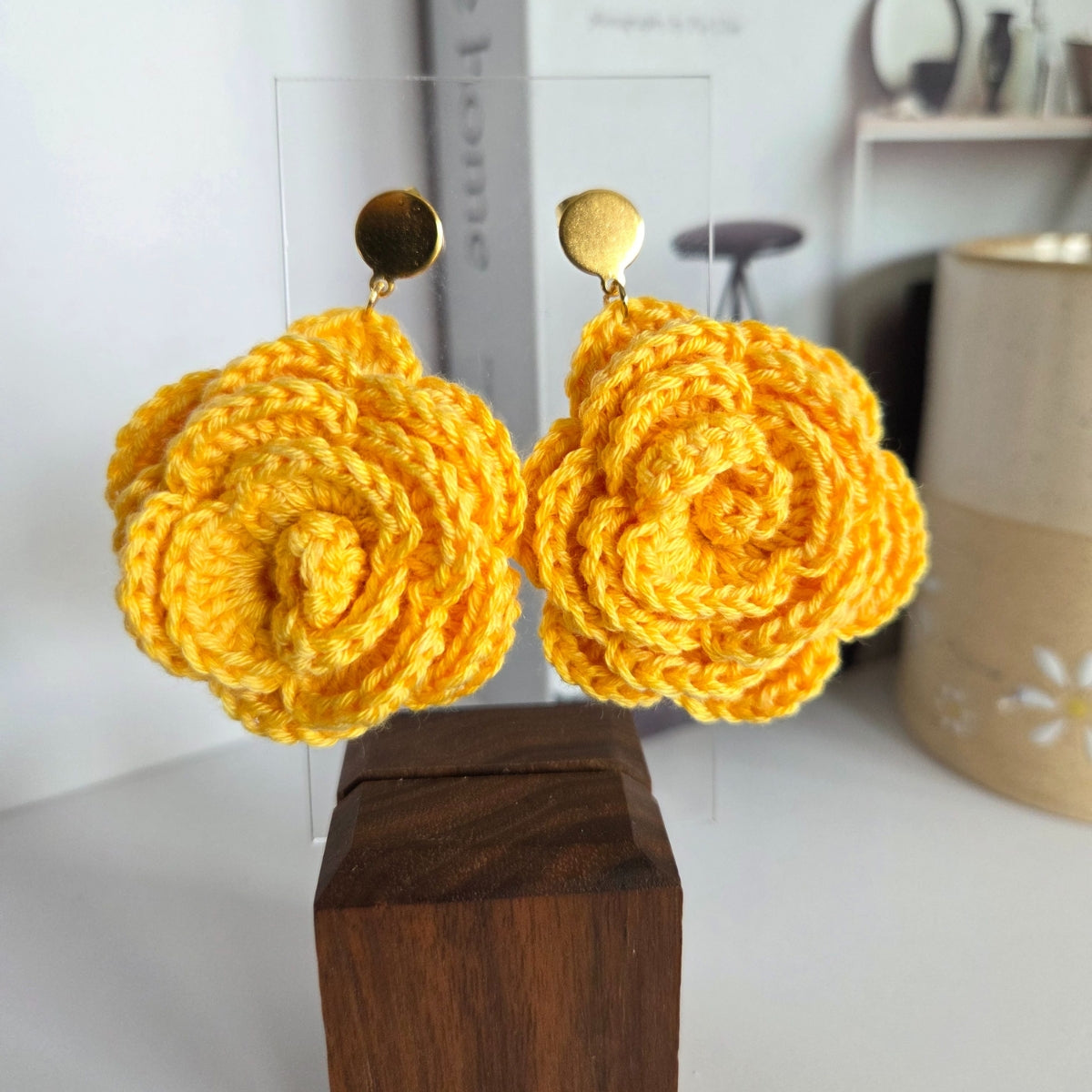 Yellow crocheted earrings on a wooden block with a blurred background