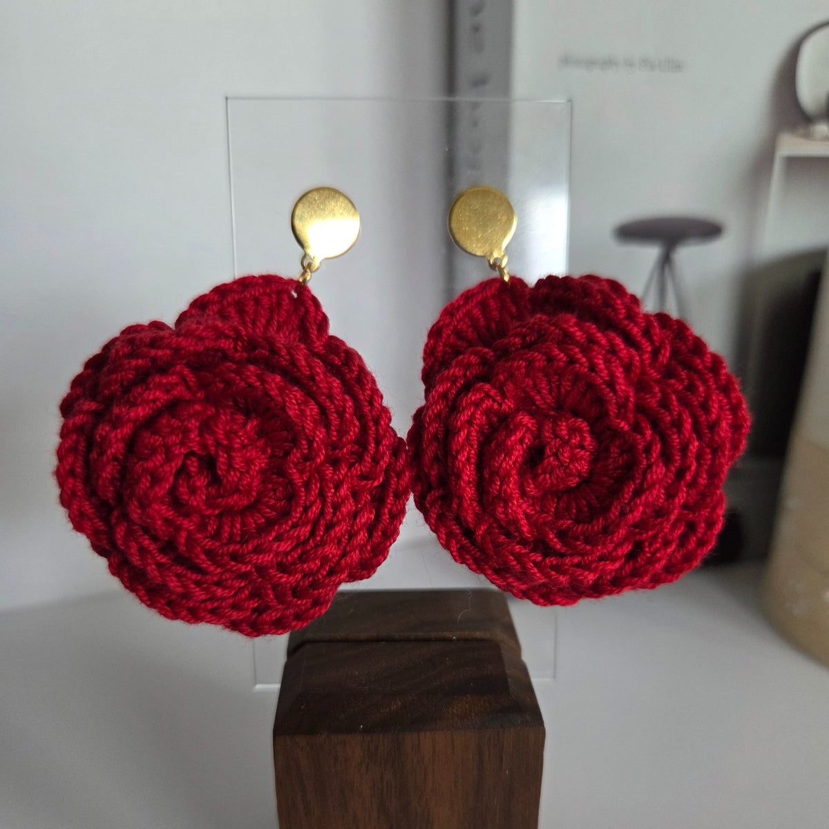 Red crocheted earrings on a wooden block with a blurred background
