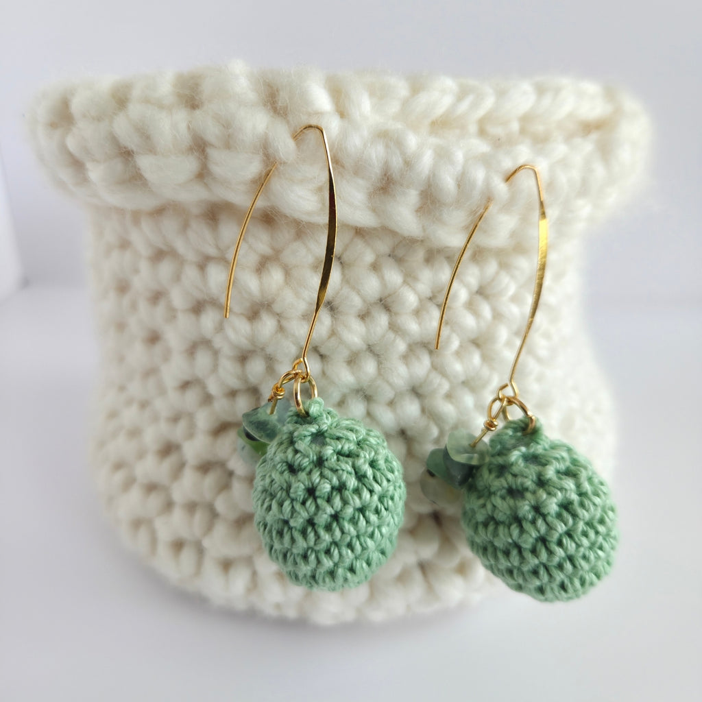 Green crocheted earrings on a crocheted basket white surface