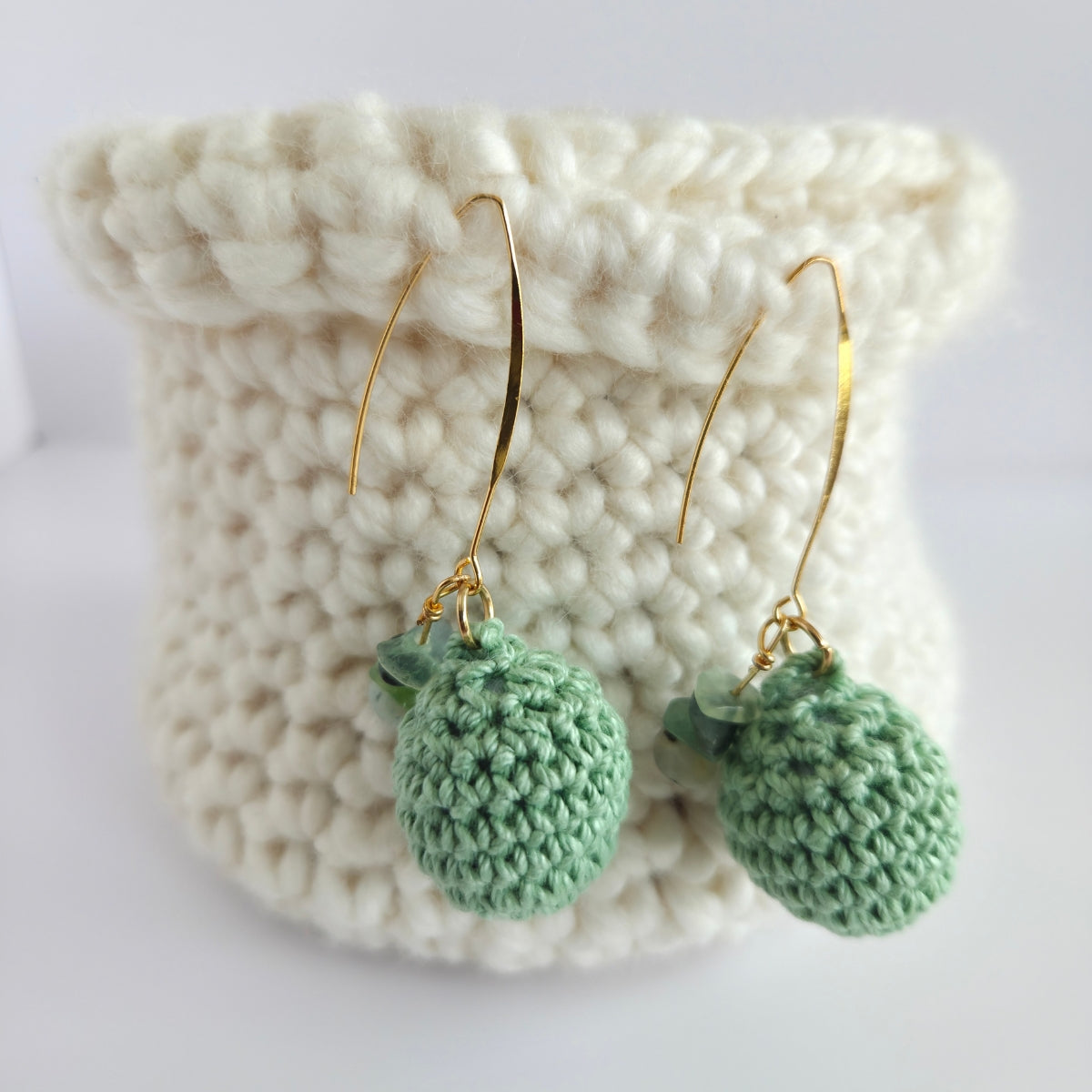 Green crocheted earrings on a crocheted basket white surface