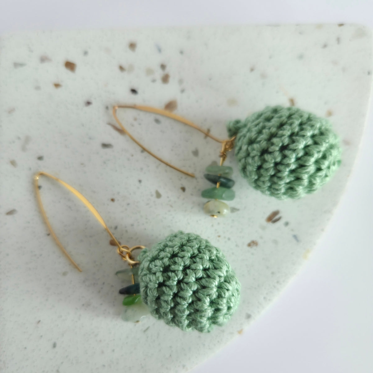 Sage green crocheted earrings on a textured marble surface.