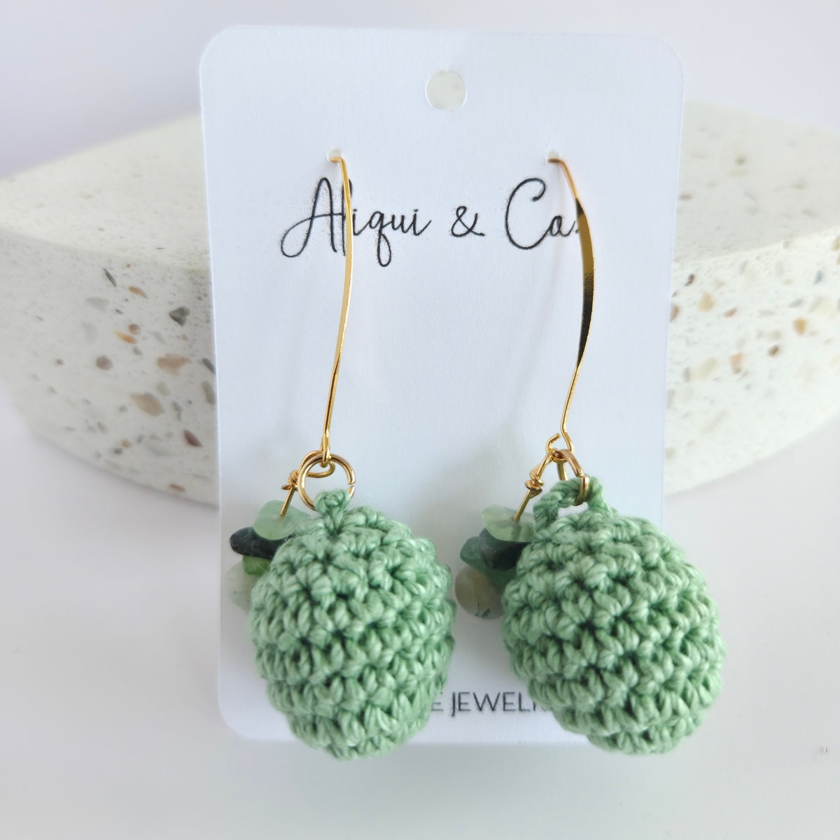 Green handmade crocheted earrings on a white card with 'Alqui & Co' branding.