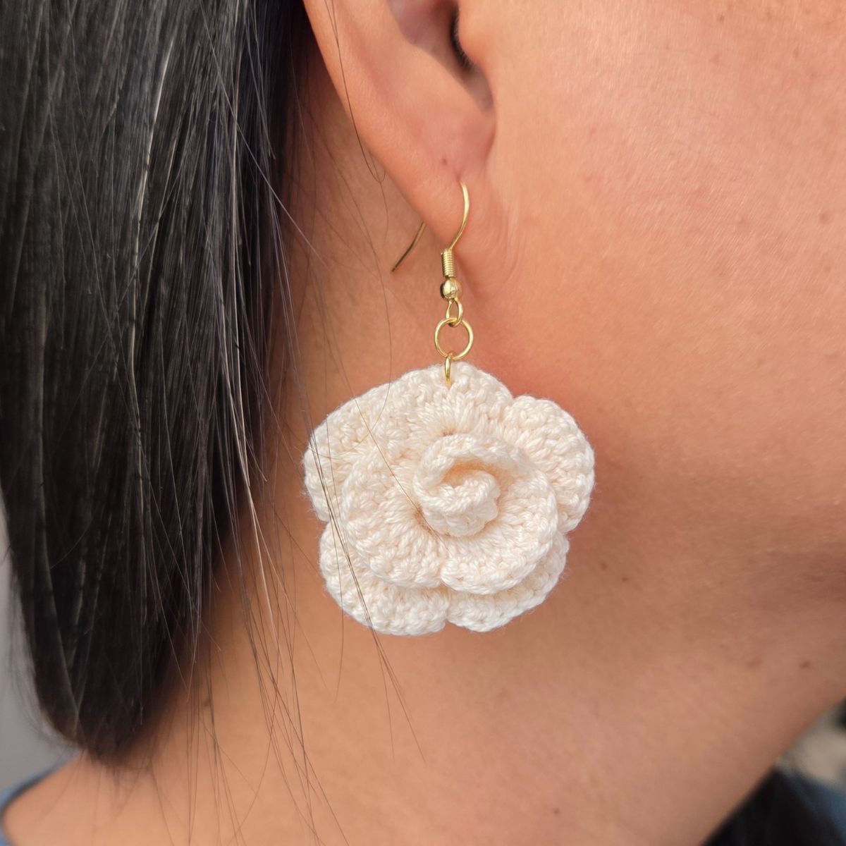 Close-up of a person wearing a white crocheted flower earring.