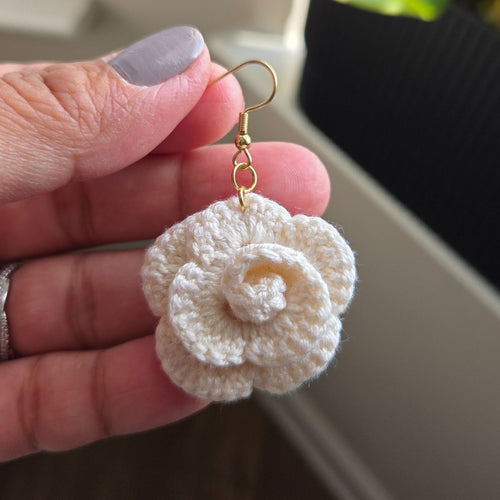 White crocheted flower earring held between fingers against a blurred background