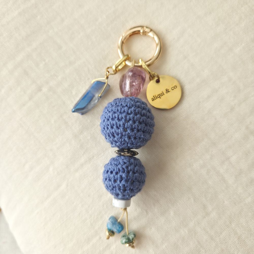 Keychain with blue crocheted beads and a gold "aliqui & co" tag on a beige background