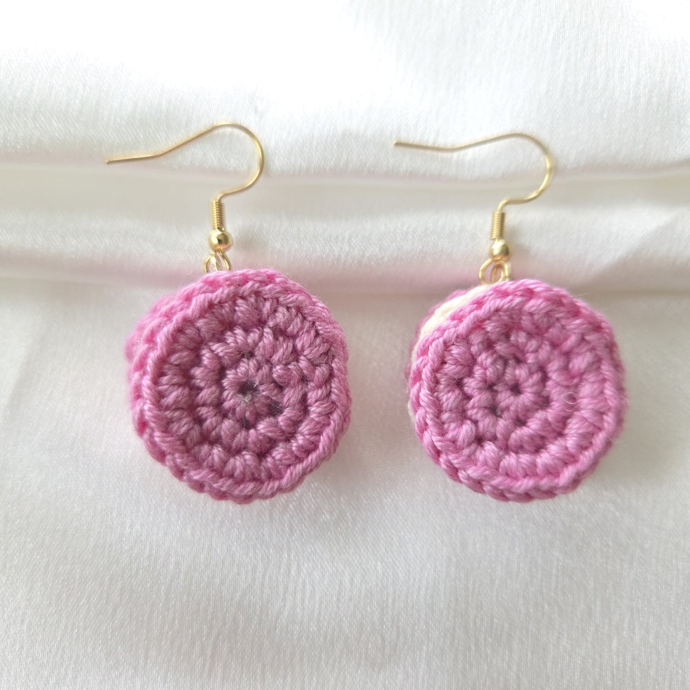 A pair of strawberry cream cookie earrings with gold fishhook wires, displayed on a soft white fabric background.