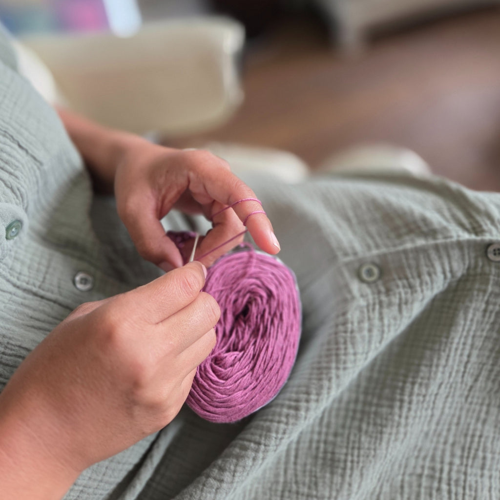 Person holding a ball of pink yarn and crochet hook in a casual setting.
