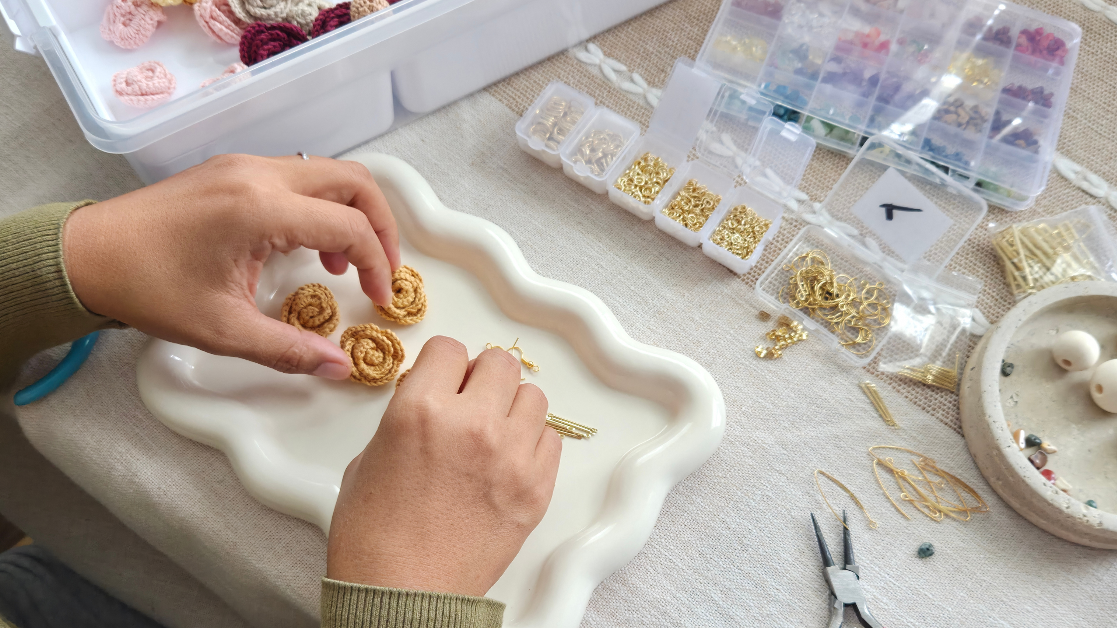 Person crafting jewelry with gold beads and tools on a table.