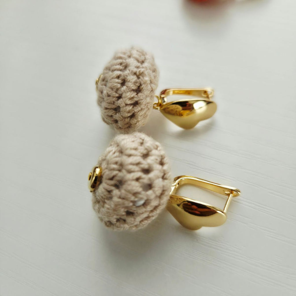 A pair of gold-toned heart lever back earrings with round,  beige crochet  displayed on a light gray surface.