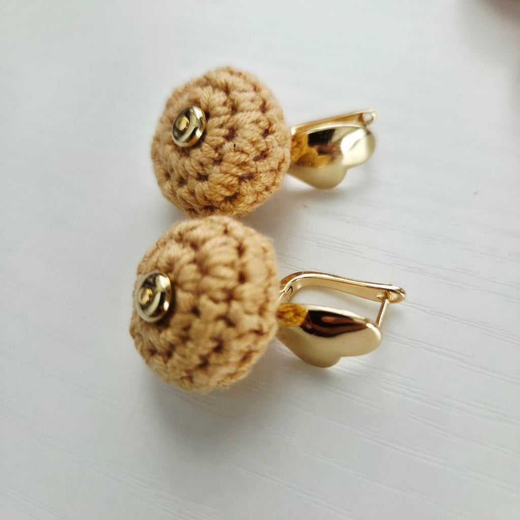 A pair of gold-toned leverback earrings with round, yellow crocheted heart studs, displayed on a light gray textured surface.