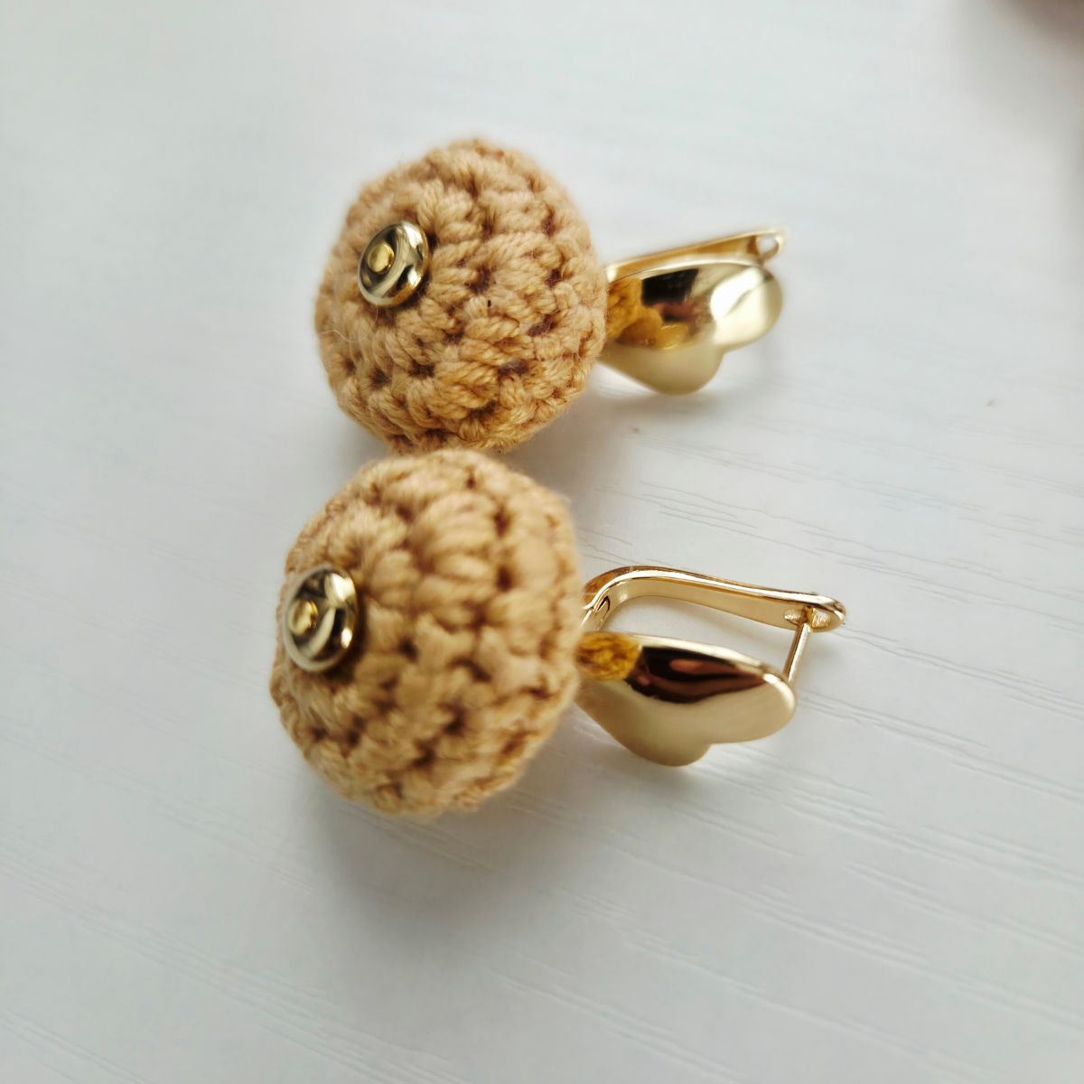 A pair of gold-toned leverback earrings with round, yellow crocheted heart studs, displayed on a light gray textured surface.